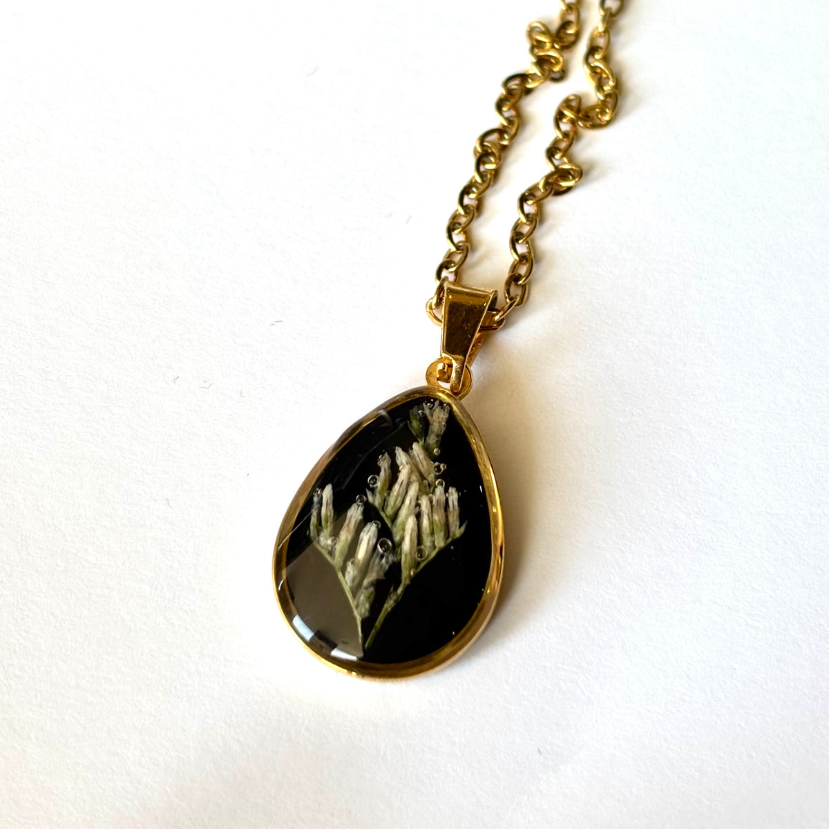 Bloomsake Clara Necklace gold teardrop pendant with preserved white botanical flowers in dark resin, angled view.