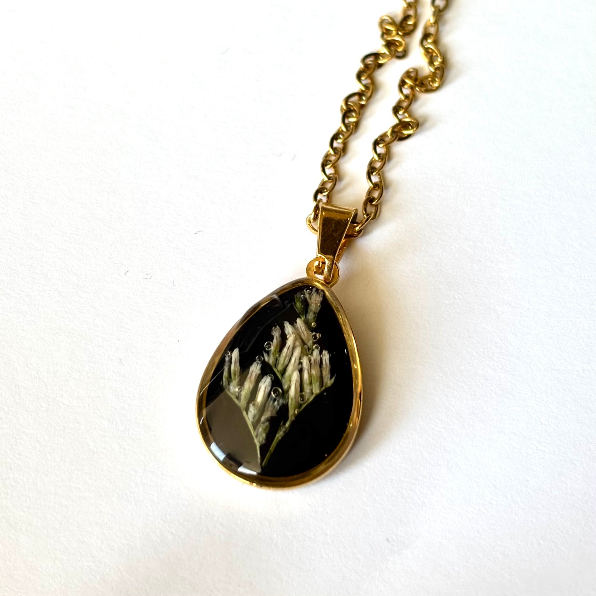 Bloomsake Clara Necklace gold teardrop pendant with preserved white botanical flowers in dark resin, angled view.