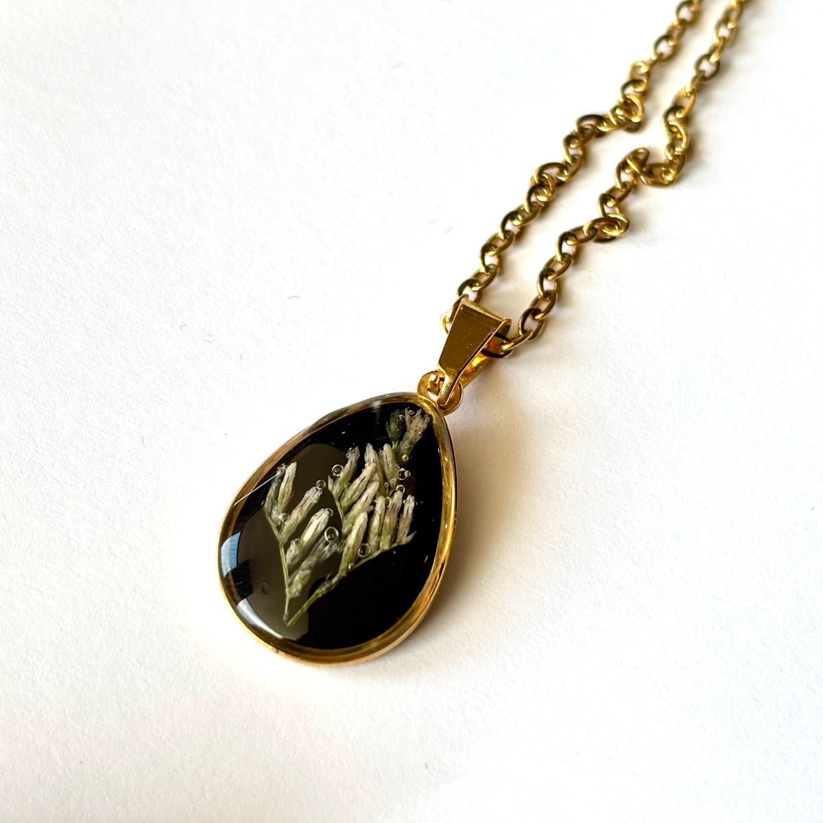 Close-up of Bloomsake Clara Necklace gold teardrop pendant showing preserved white flowers in dark resin.