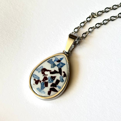 Close-up of Bloomsake Clara Necklace silver teardrop pendant showing blue and burgundy preserved flower petals in white resin.