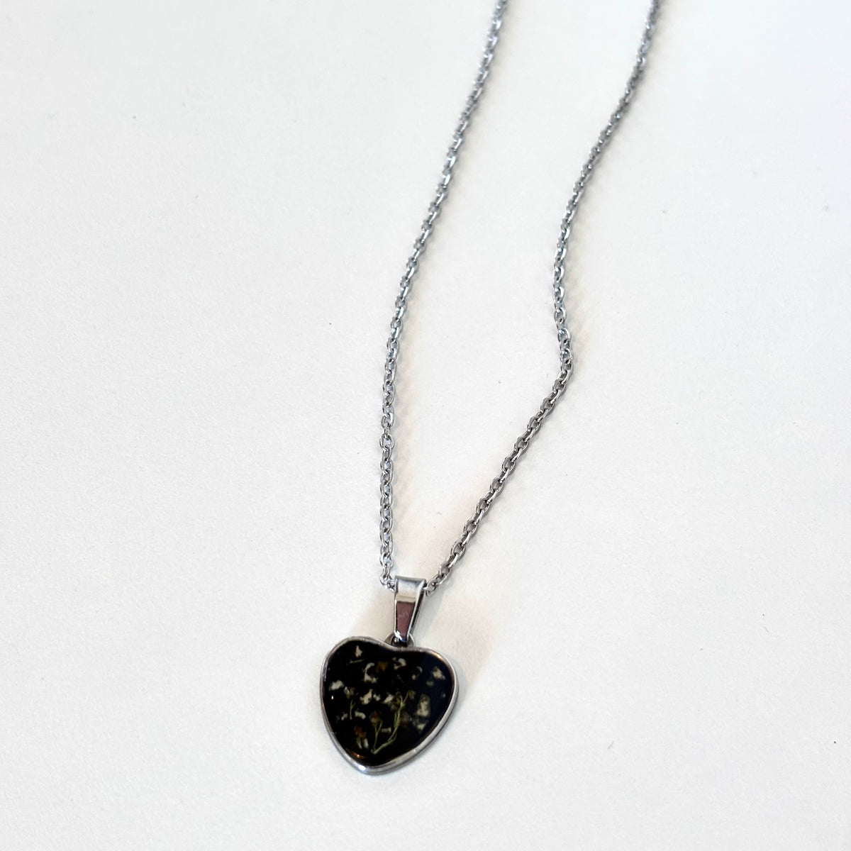 Close-up detail of Bloomsake silver heart pendant necklace showing preserved flowers in dark resin.