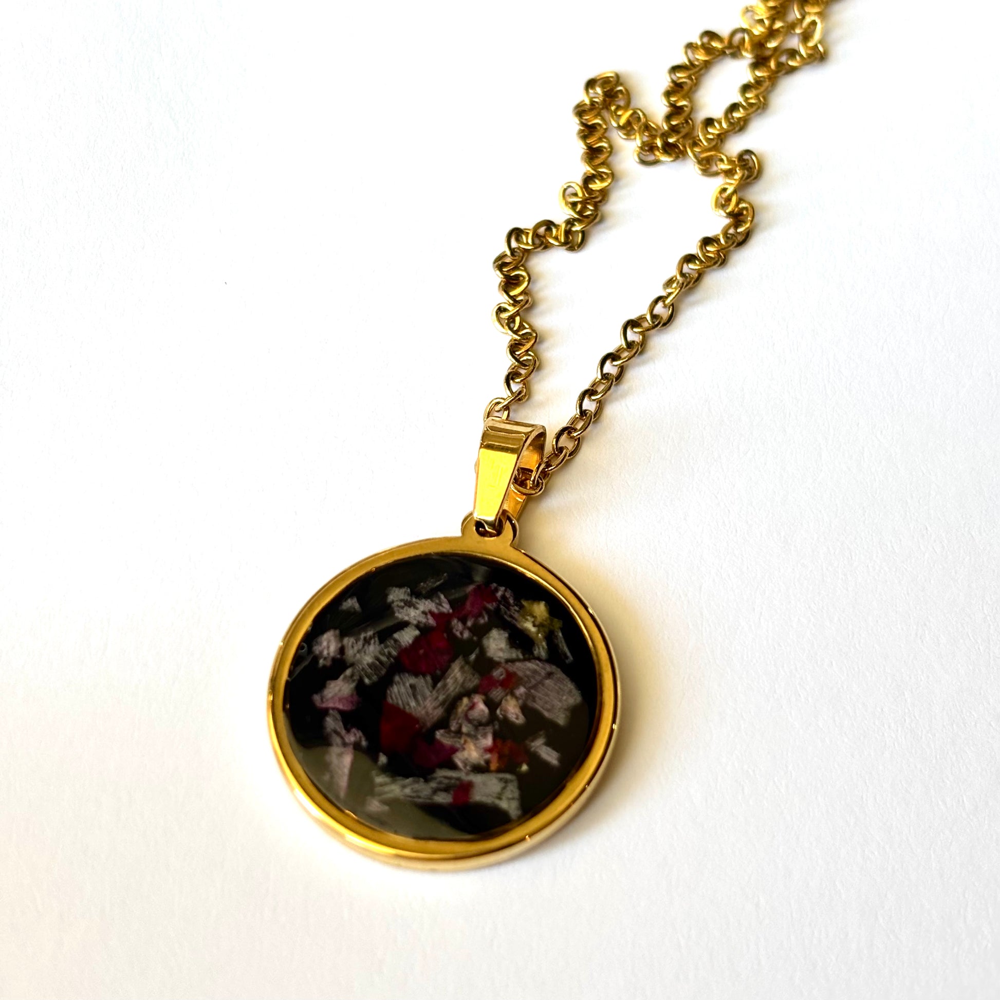 Close-up of Bloomsake Margot Necklace showing preserved flower petals in dark resin set in gold round bezel pendant.