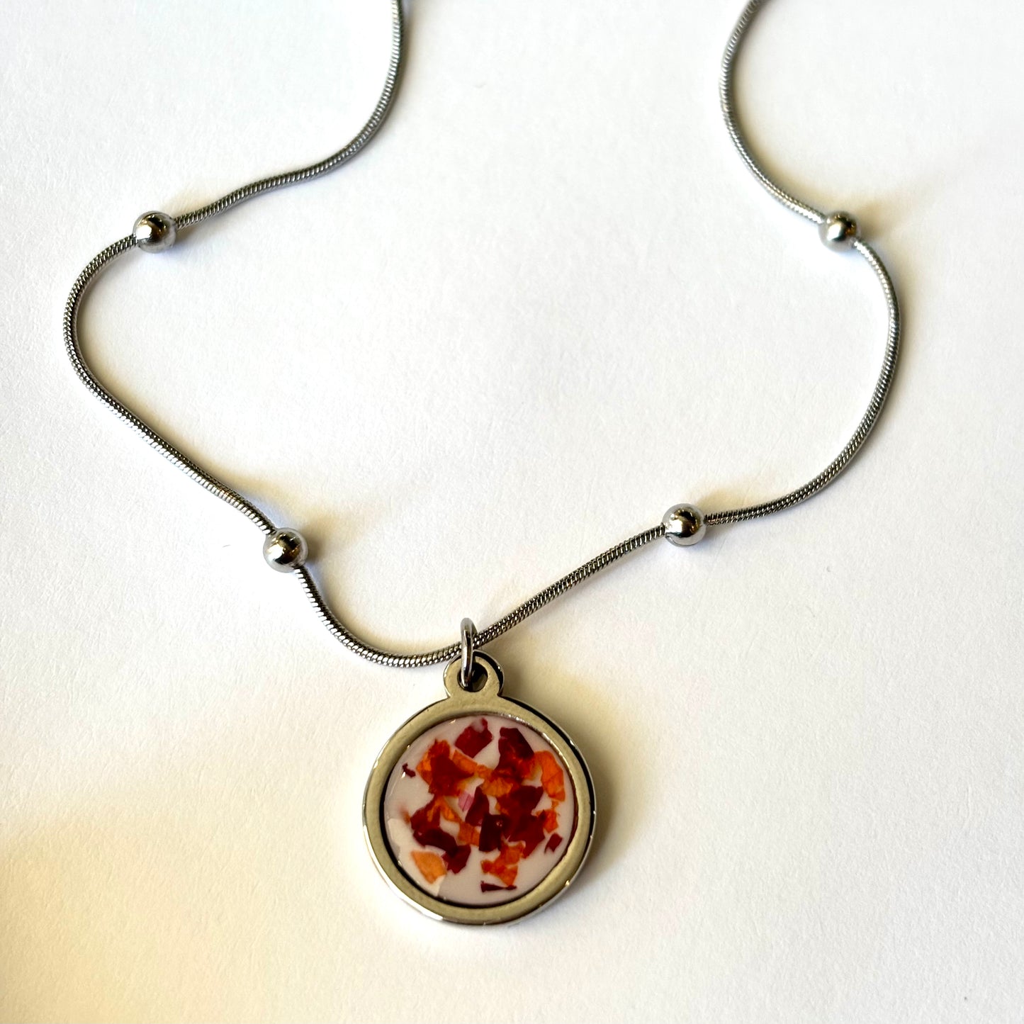 Close-up of Bloomsake Nova Necklace round resin pendant with preserved red and orange flower petals in silver setting.