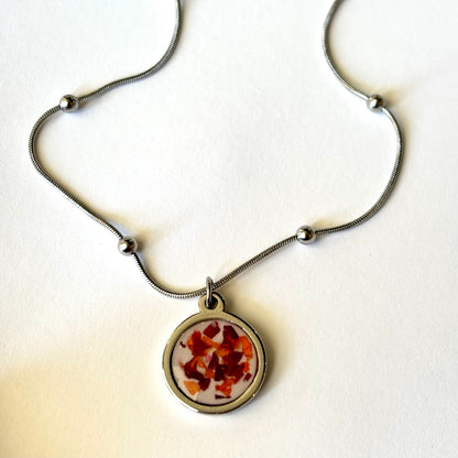 Close-up of Bloomsake Nova Necklace round resin pendant with preserved red and orange flower petals in silver setting.