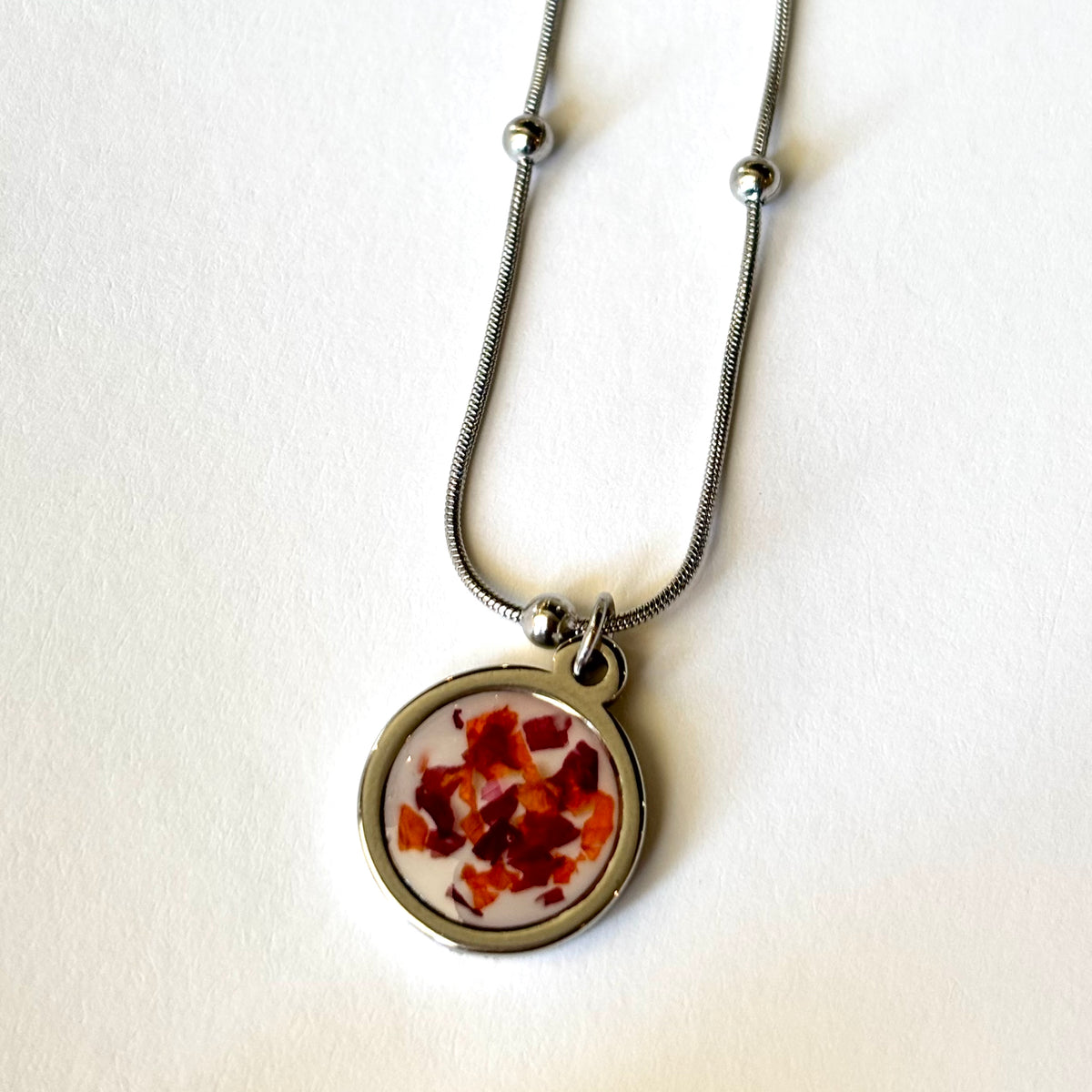 Bloomsake Nova Necklace with red and orange flower petals in white resin round pendant on silver satellite chain, full view.